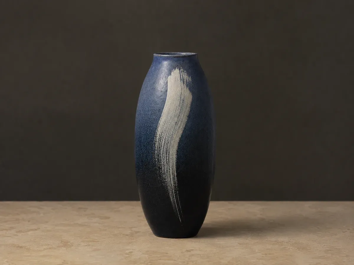 Tall indigo vase shading to near-black at the base, with a single pale brushstroke swept down the front.