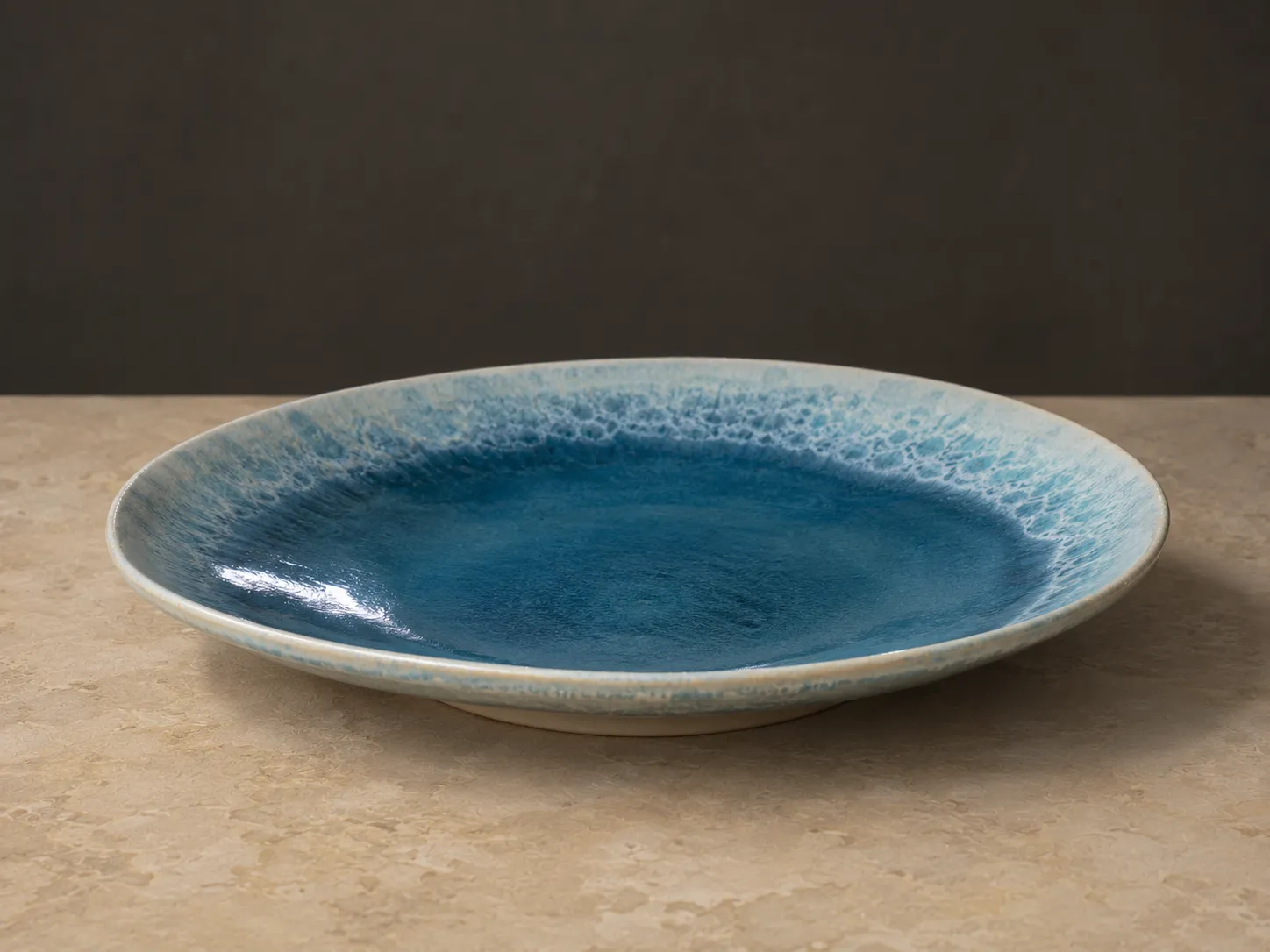 Wide serving plate glazed deep ocean blue in the well, breaking to a foamy pale rim.